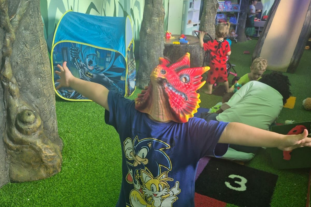 Criança de máscara de dragão com os braços abertos, brincando no Bosque dos Sonhos