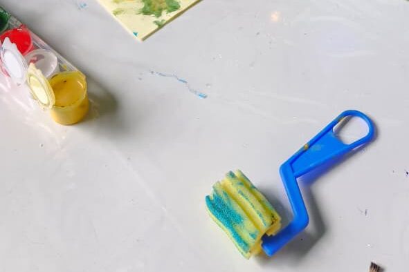 Rolinho de pintura e potes de tinta sobre a mesa da oficina